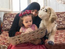 A young girl reading a book with her grandmother and a puppet