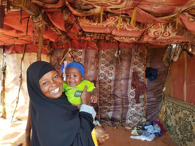 beeso in a tent holding her baby and smiling