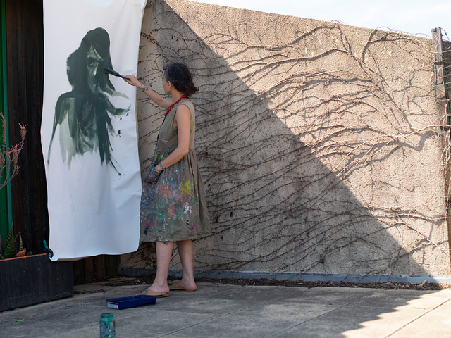 Diala paints a picture on a large sheet of paper hanging on the wall outside