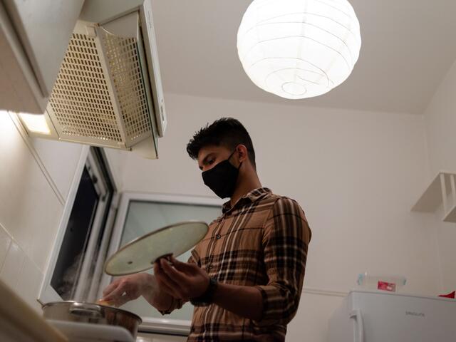 Young man in a kitchen cooking while wearing a face mask