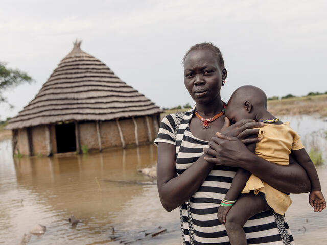 A mother holding her sleeping baby in front of their flooded house in South Sudan