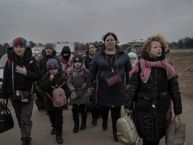 A large group of Ukrainian refugees walking outside carrying bags