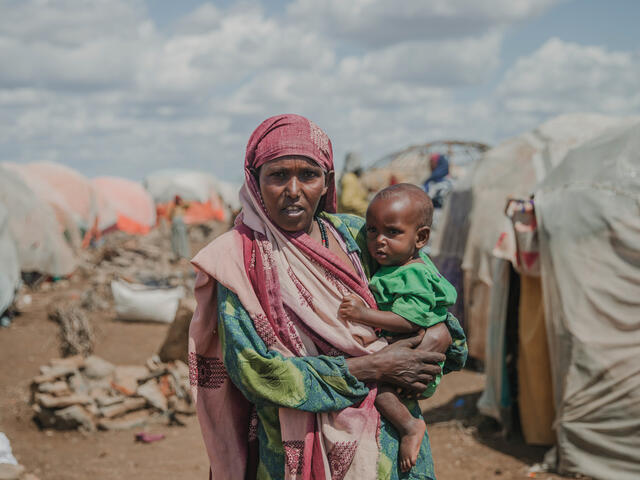A Somali mother holders her 1 year-old baby in front of tents at a camp for internally displaced people