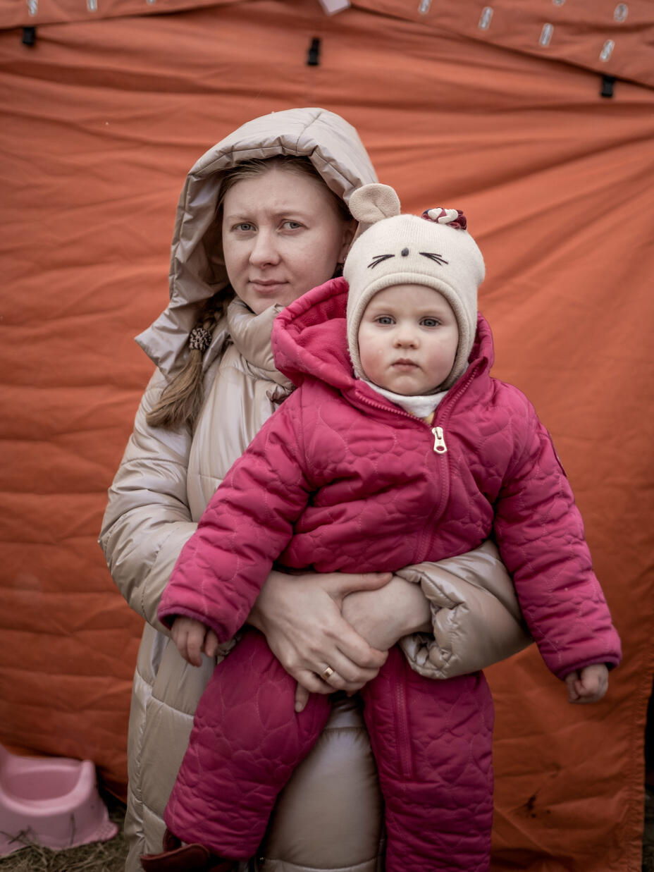 Iryna carries her daughter who wears a pink snowsuit