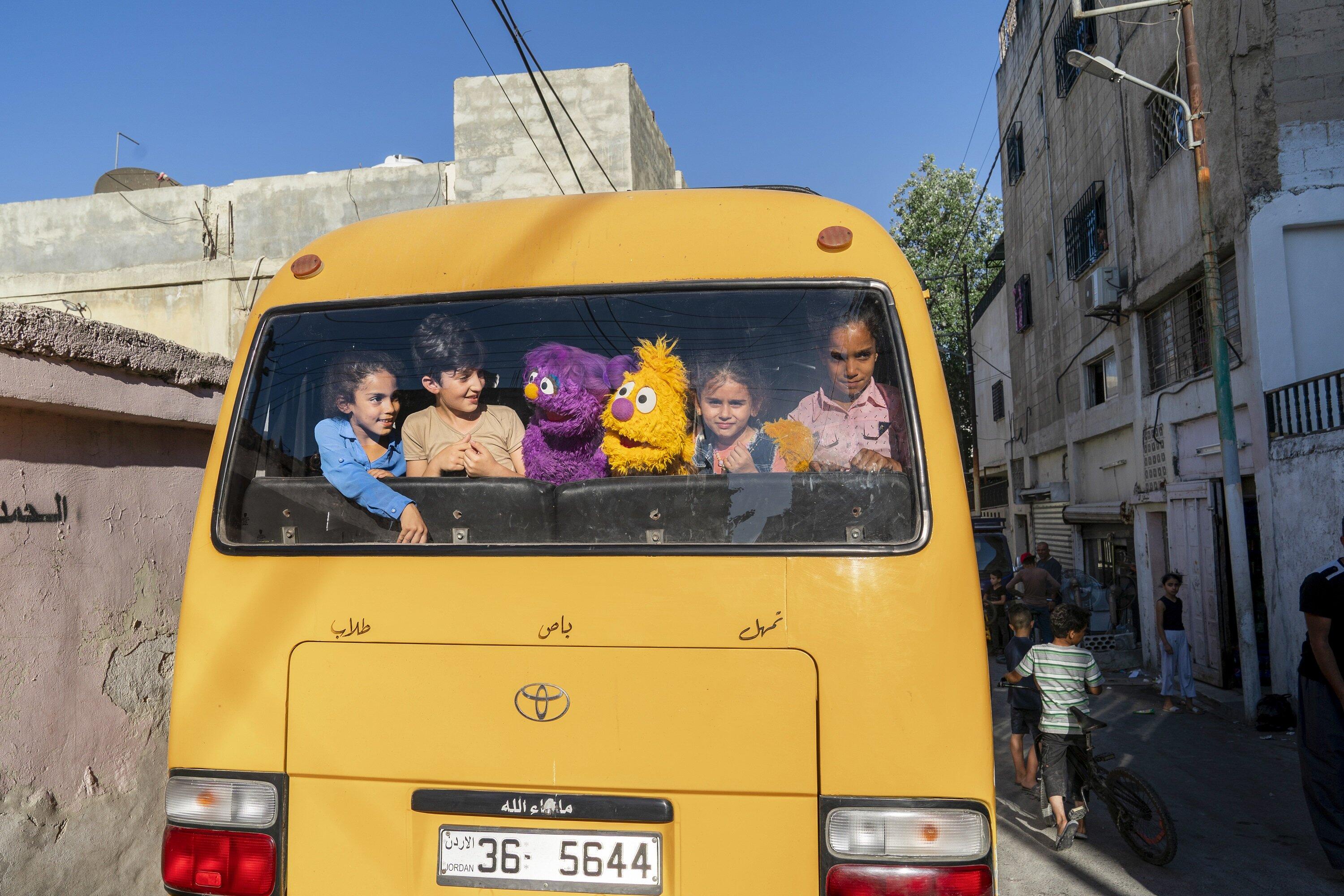 Kids and sesame street puppets looking out of the back window of a bus
