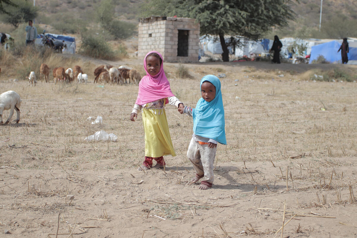 Two young children holding hands, walking in village surroundings