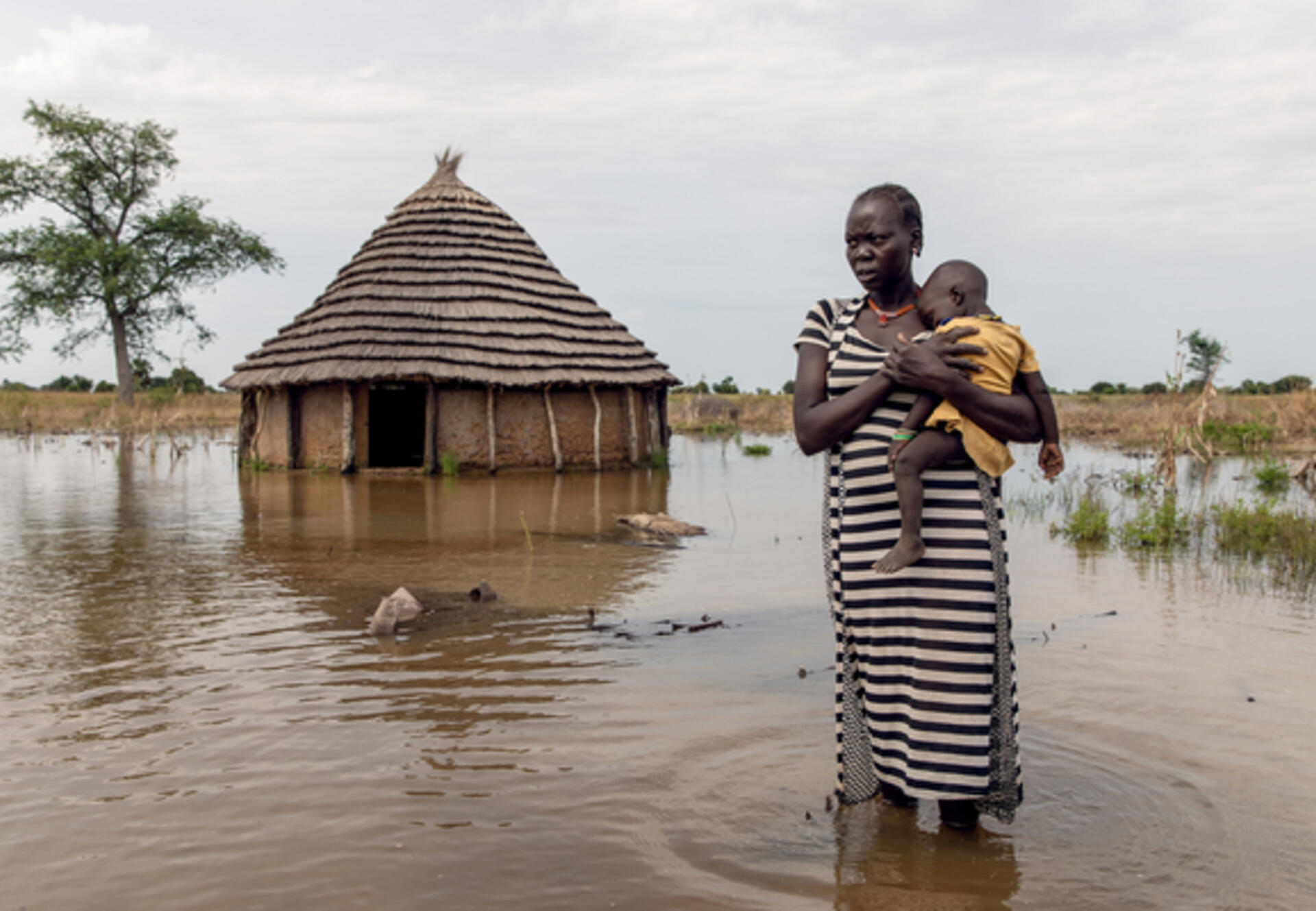 A mother carries her baby amidst flooding in South Sudan