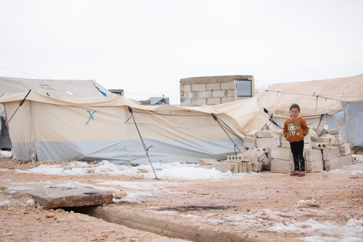 Little girl standing in front of her family's makeshift tent in a refugee camp in Syria.