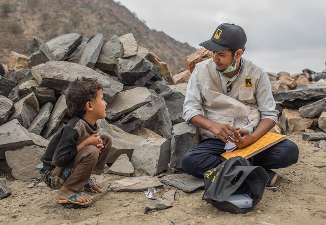 An IRC employee sitting with a young boy in front of rubble