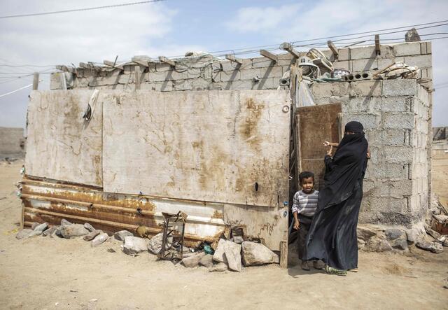 A woman stands in front of a house together with her little son