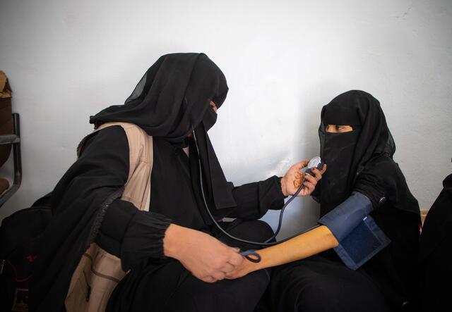 two fully veiled women, one taking the blood pressure of the other