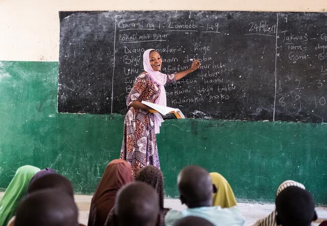 A woman standing in front of a class and pointing to some text on the board
