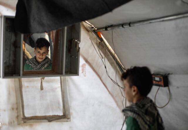 Ten year old Omar looks in the mirror in a tent