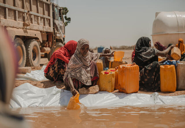 A 40-year-old woman in Ethiopa leans over to scoop water out of a reservoir with other women putting water in their plastic jerry cans.
