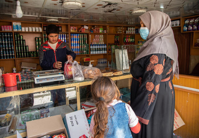 Noor* takes her daughter to the local market to purchase food for her and her children using the emergency cash assistance provided to her by the International Rescue Committee.