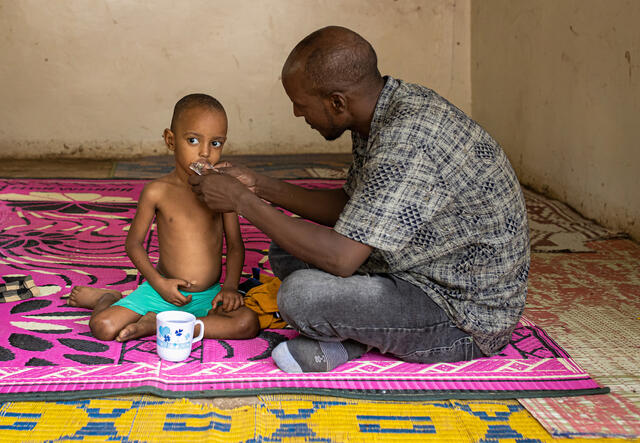 A man feeds his son during a screening for malnutrition at Locher Angamor Health Dispensary in Kakuma Refugee Camp, Turkana, Kenya