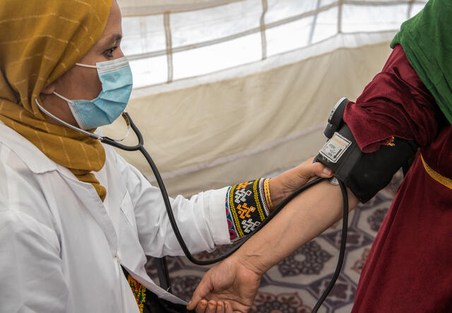 An Afghan female mobile health worker takes a woman's blood pressure