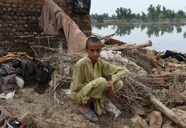 Faisal* tries to smile as he sits in the demolished house with no shelter with his family in Pakistan.