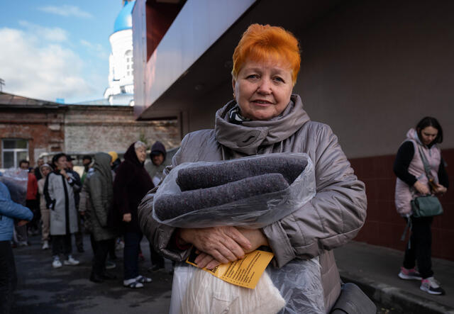 Lyubov faces the camera, holding a blanket.