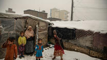 An Afghan family huddles in the snow outside their makeshift house
