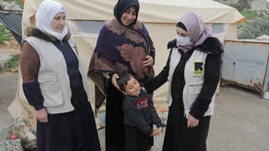 An IRC worker talking to Syran women and a young child