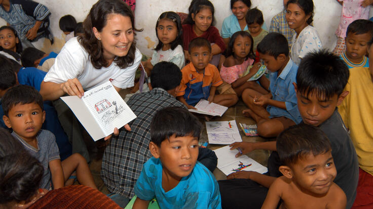 a woman handing out papers to a big group of children
