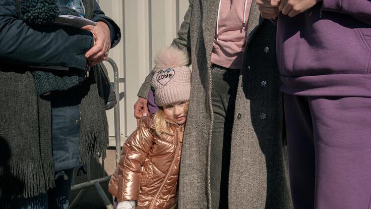 A child in a pink coat and hat hugs her mother after fleeing Ukraine