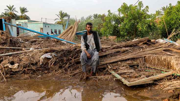 A man sits by a destroyed shack in a flooded area in Sudan